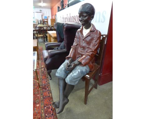 A life size Goldscheider style hand painted fibreglass figure of a seated young boy 