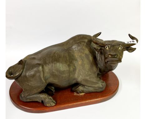 A Chinese bronze coloured terracotta figure of a water buffalo on a wooden pedestal, L. 46cm.