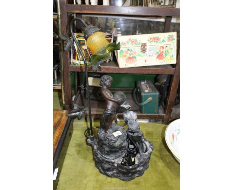 A small contemporary Table Lamp with water feature depicting a boy pouring an urn over a cascade of plants, with green shade,