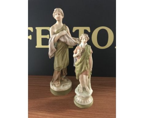 TWO ROYAL DUX CLASSICAL FIGURE ORNAMENTS of graduated size, painted in pastel tones with gilt highlights, set on circular bas