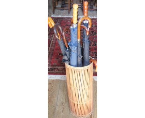 A woven cane stick stand, containing a collection of gentleman's umbrellas, one by Brigg.