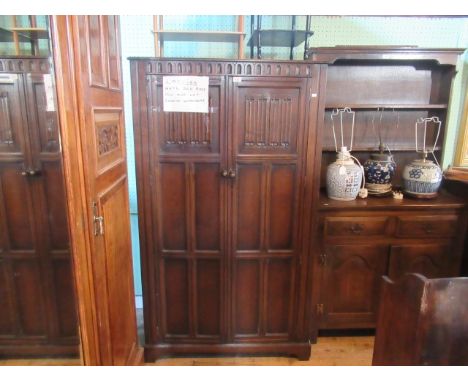 A reproduction lady's wardrobe, having a thumb moulded frieze over a pair of linen fold panelled doors, enclosing shelves and