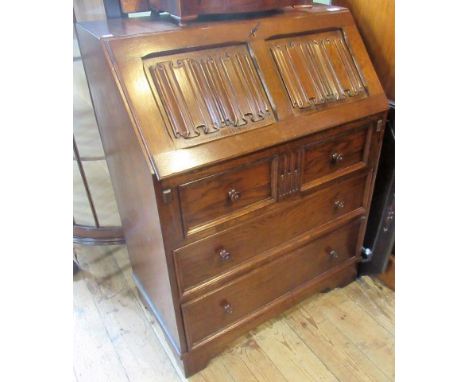 A reproduction oak bureau, having a linen fold panel fall, enclosing a fitted interior over three graduated long drawers on b