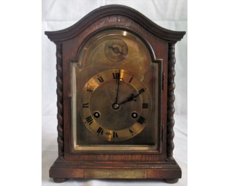An early 20th century oak cased eight day mantle clock with arched top and spiral pilasters, the brass dial with applied chap