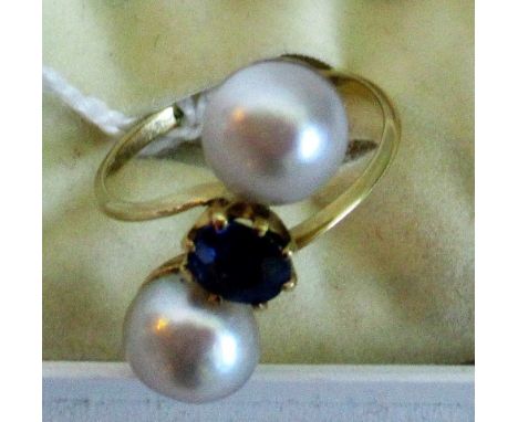 A sapphire and pearl crossover ring, the oval circular set sapphire in a claw mount, flanked by cultured pearls to a plain sh