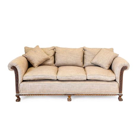 An Early 20th Century Carved Mahogany Three Piece Suite, upholstered in light-brown fabric, comprising a three-seater sofa wi