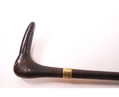 A wooden walking stick with brass collar, the handle being a carved long beaked bird