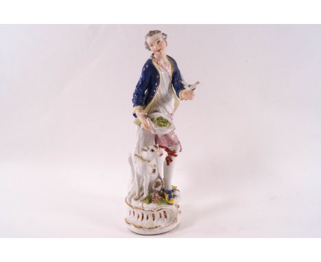 A Meissen figure of a man in a blue jacket holding a bird, his hat with a nest at his waist and a hound at his feet, crossed 