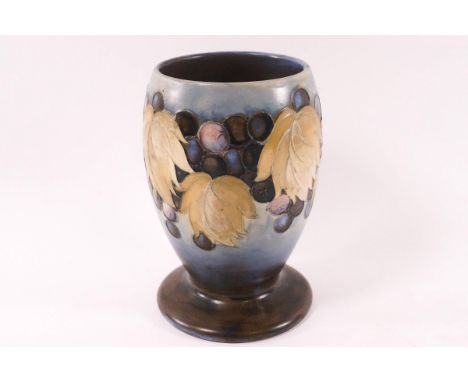 A Moorcroft pottery salt glaze footed vase, decorated wtih grapes on a blue ground, factory marks, 15cm high