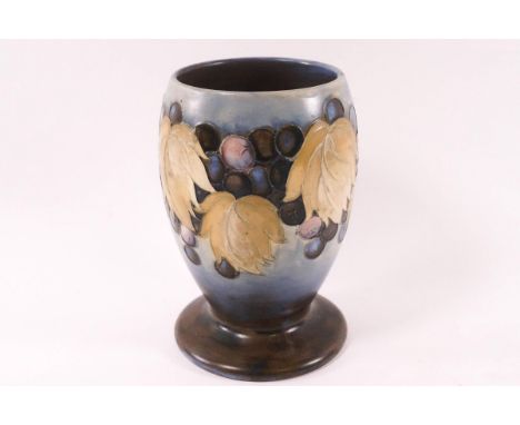 A Moorcroft pottery salt glaze footed vase, decorated wtih grapes on a blue ground, factory marks, 15cm high