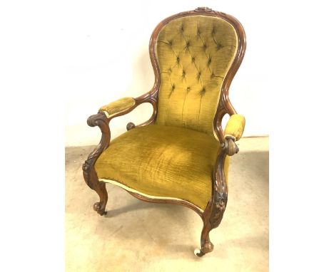 A wide seated Victorian button back arm chair with carved arms on brass and ceramic castors. W:70cm x D:83cm x H:99cm