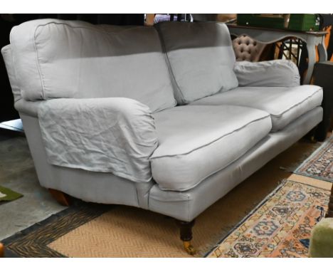 A Howard style three seater sofa, turned mahogany front legs with brass castors, pale blue upholstery (a/f), 220 cm w x 95 cm