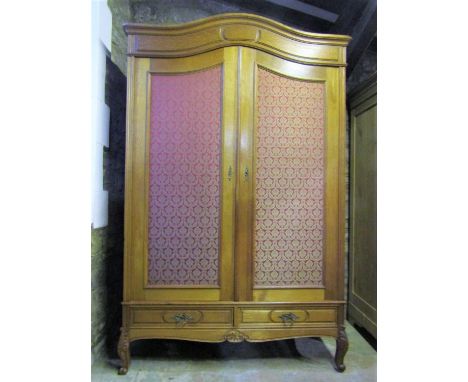 A medium to light oak armoire with moulded arched cornice over a pair of three quarter length  material covered panelled door