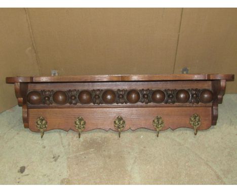 An oak wall mounted hall shelf and combined hat/coat rack with repeating carved and moulded frieze over five cast hooks with 