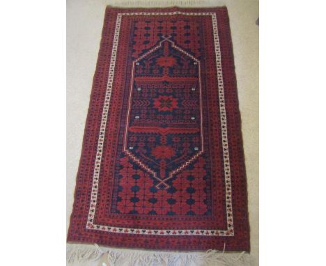 An Afghan red ground carpet upon an ink blue field with repeating red floral detail within running borders, 190 x 105 cm appr