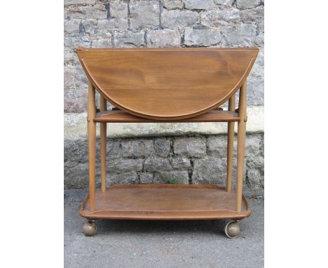 An Ercol medium elm and beechwood three tier drop leaf tea trolley together with a contemporary beechwood three tier kitchen 