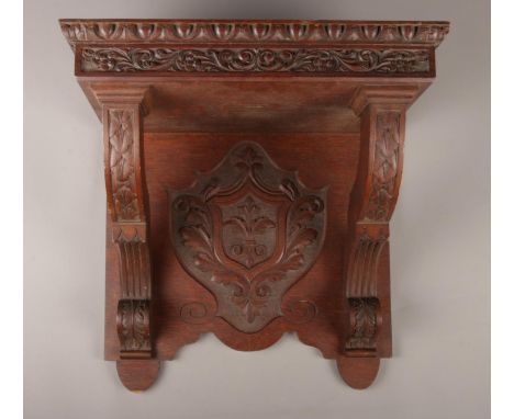 A large carved oak wall shelf, with crest to the underside and floral and foliate border. Height: 43cm, Width: 46cm, Depth: 3