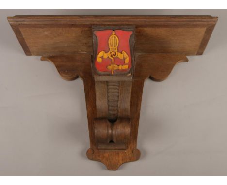 A carved oak clock bracket, with central coat of arms and scrolls to the side.  