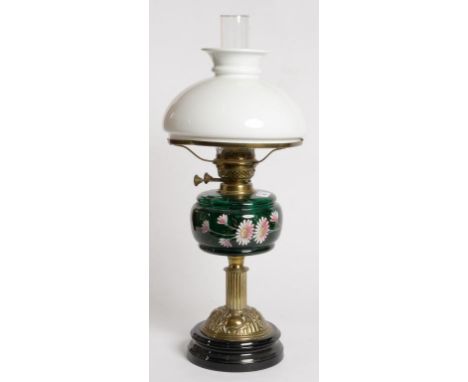 AN EDWARDIAN EMBOSSED BRASS OIL LAMP, THE GREEN GLASS FOUNT ENAMELLED WITH MICHAELMAS DAISIES, BRASS BURNER, ON BLACK GLAZED 