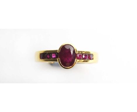 A ruby dress ring, the central oval facet cut ruby flanked by six circular facet cut rubies in channel setting, on yellow met