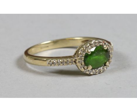 A 9ct gold ring set with an ovoid faceted emerald under a diamond surround and shoulders, size M.