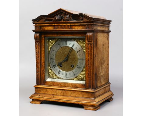 A carved figured walnut mantel clock with square brass dial ornamented with spandrels and a silvered chapter ring. Housing an