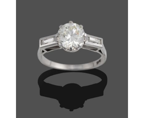 A Diamond Solitaire Ring, the round brilliant cut diamond claw set between shoulders each inset with a baguette cut diamond, 