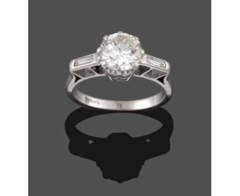 A Diamond Solitaire Ring, circa 1930, a round brilliant cut diamond in white claws with a baguette cut diamond set into each 