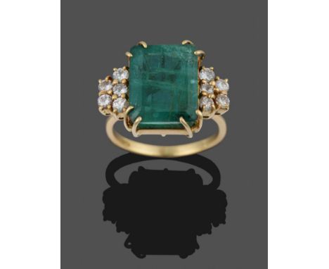 An Emerald and Diamond Ring, the emerald-cut emerald flanked by five round brilliant cut diamonds either side in yellow claw 