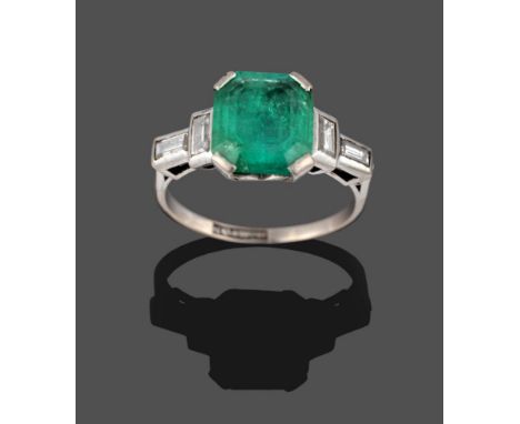 A Mid 20th Century Emerald and Diamond Ring, the emerald-cut emerald in a white corner claw setting, with two baguette cut di