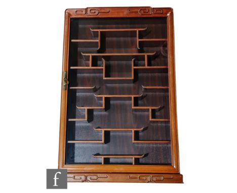 A Chinese hardwood snuff bottle cabinet, the glazed front cabinet with hinged door revealing a series of traditional scroll s