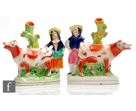 A mirrored pair of Staffordshire spill vases modelled as facing cows with a lady and gentleman stood behind with a tree trunk
