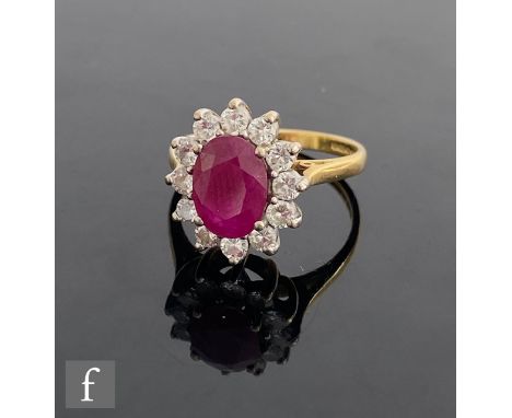 An 18ct hallmarked ruby and diamond cluster ring, central oval ruby, length 10mm, within a border of twelve brilliant cut dia