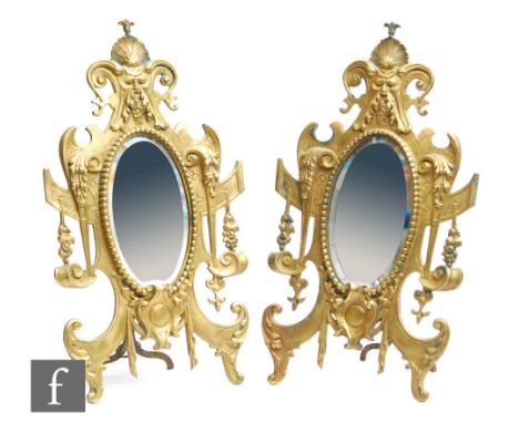 A pair of early 20th Century gilt metal easel back mirrors, each of the bevelled oval mirror plates inset within cast and pie