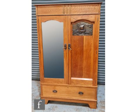 An Arts and Crafts oak wardrobe, the cornice pediment above double doors with a mirror panel and repousse work copper panel d