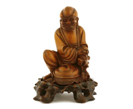 A Chinese boxwood carving, Qing dynasty (1644-1911), of a luohan wearing a robe with scrolling borders, seated leaning toward