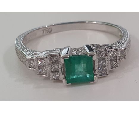 An 18ct white gold emerald and diamond Art Deco ring. The ring with central emerald cut emerald on stepped diamond shoulders 