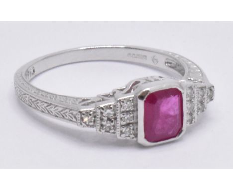 An 18ct white gold ruby and diamond Art Deco ring. The ring with central emerald cut ruby on stepped diamond shoulders to pla