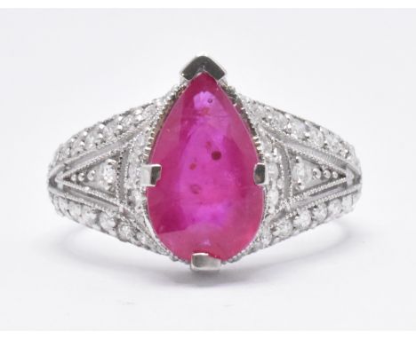 An 18ct white gold and ruby dress ring. The ring having a pear cut ruby to the centre with round cut diamond accent stones to