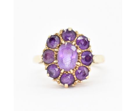 A hallmarked 9ct gold and amethyst cluster ring. The ring having a central oval cut amethyst surrounded by eight further roun