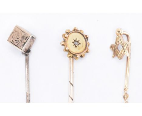 A group of three gold stick pins to include one having a masonic symbol finial, one having an engraved cube finial and one ha