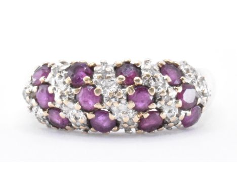 A hallmarked 9ct gold ruby and diamond ring. The ring being set with twelve round cut rubies with diamond accent stones set i