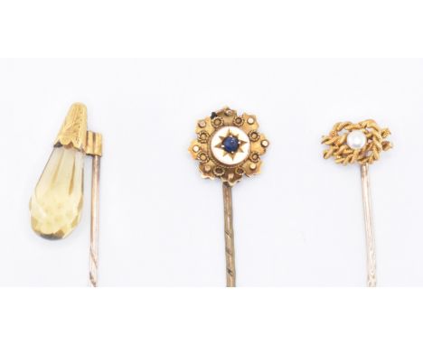 Three gold stick pins to include a briolette finial pin, a knot design pin set with a pearl and a Victorian blue stone set pi