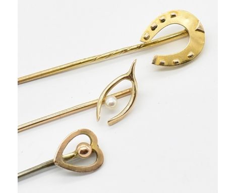 Three gold stick pins to include a 15ct gold horse shoe stick pin, a 15ct gold pearl wish bone stick pin and a white metal pi