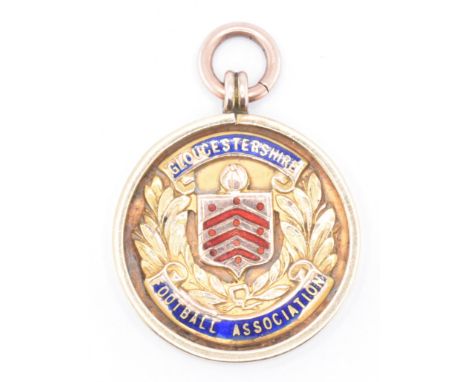 A 1930s hallmarked 9ct gold Gloucestershire football association medal. The medal of round form with enamelled coat of arms t