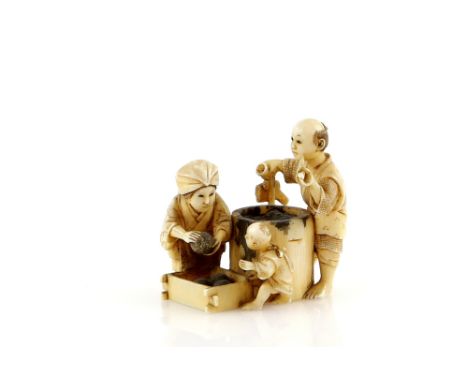 An ivory netsuke or small okimono, carved as a small family making rice balls; the man with a pipe in his left hand, signed H