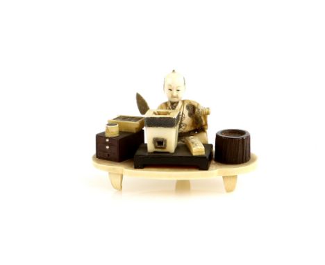 A sectional ivory okimono carved as a seated artisan, holding a mason's trowel with his right hand; on a shaped oval base, ne