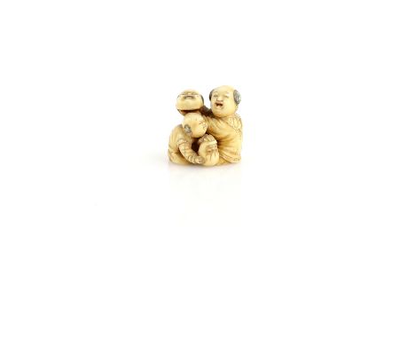An ivory netsuke carved as two boys with an Okame mask and a Daruma doll, two kanji on the base, 19th or 20th CenturyProvenan