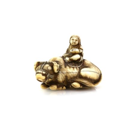 A very fine ivory netsuke by Masanao of Kyoto, carved as an acolyte, or other figure, seated on the back of a recumbent water