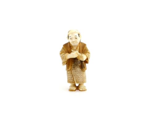 A stained ivory netsuke of a standing man, holding a pipe and pipe case, signed Kozan, 20th  CenturyProvenance: The Property 